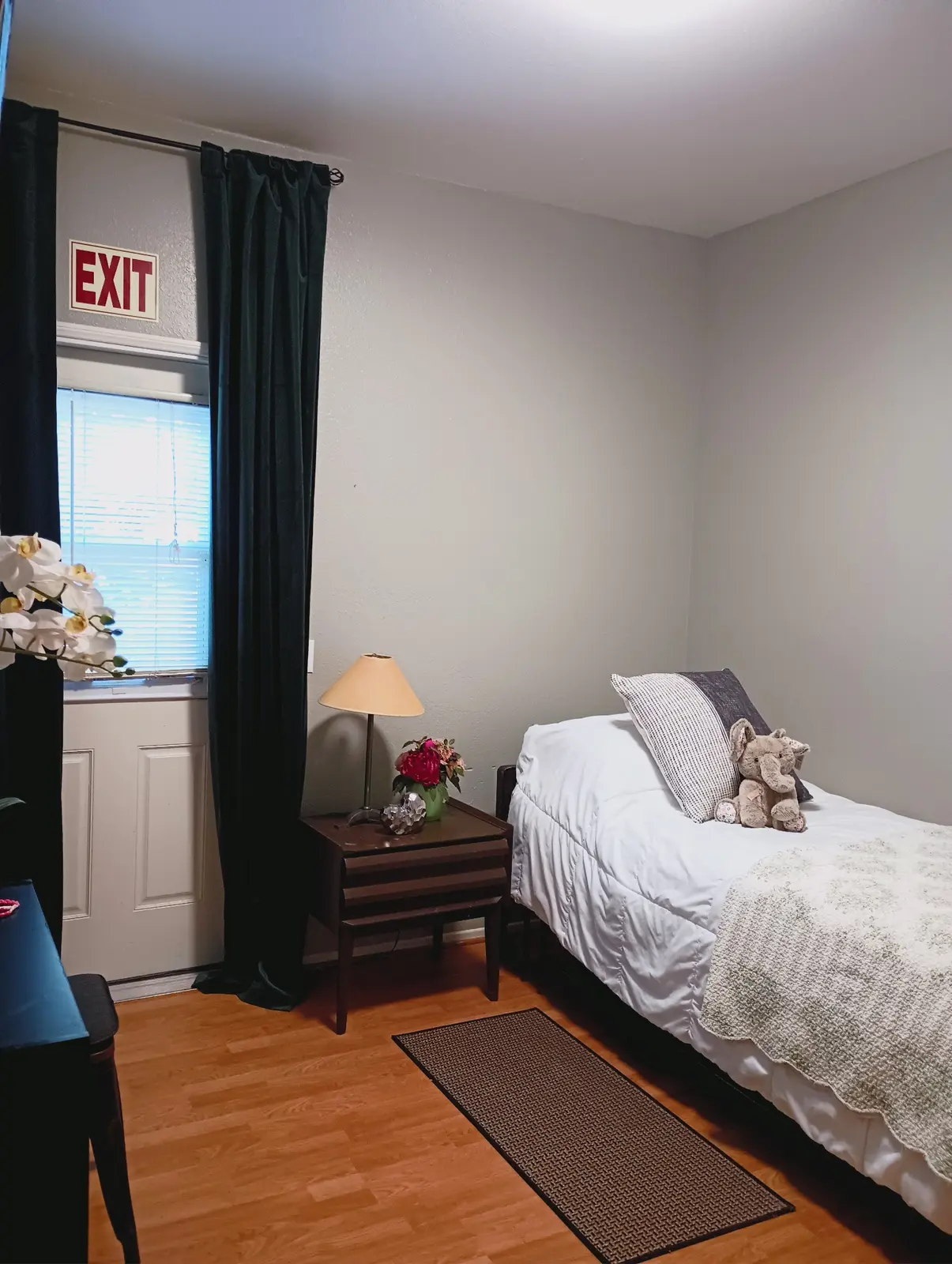 Single private room with a neatly made bed, bedside table, and private exit